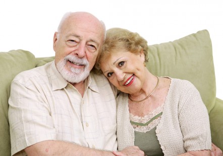 Picture of a couple in their 70s looking happy and sitting on a green sofa together
