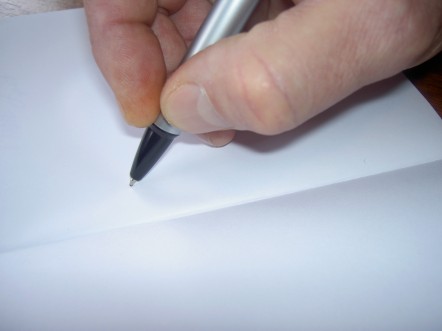 close up of a hand writing with a silver pen on a white notebook