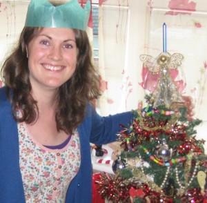 Woman wearing paper hat standing next to a Christmas tree