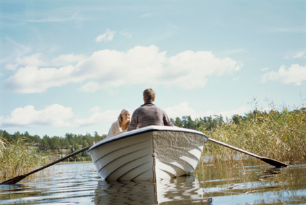 A man and a woman in a white row boat on a river on a sunny day