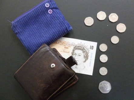 A wallet and a purse on top of a ten pound note and question mark made of coins