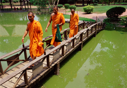 Three Buddhist Monks walking across a wooden bridge