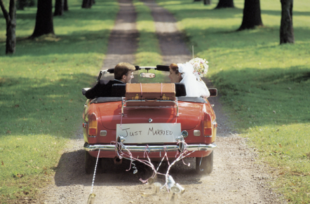A man in a suit and woman in a wedding dress in a red convertible with just married written on it