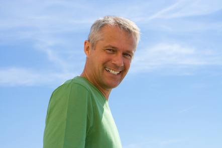 Grey haired man in green t-shirt smiling against blue sky