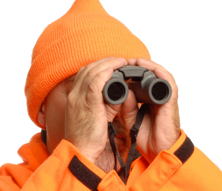 Man in orange hat and coat looking through binoculars