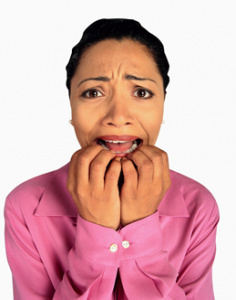 Woman in a pink blouse biting her nails.