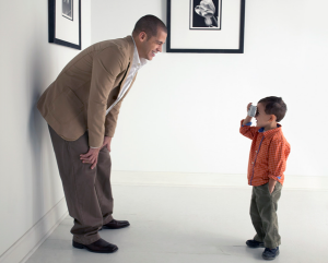 A young boy taking a photo of a man in a beige suit