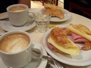 Two coffees and two plates of croissants with cheese and ham.