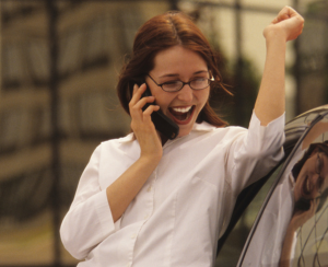 Woman in white shirt talking on a mobile phone next to a car.