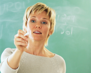 Blonde woman holding chalk in front of a green chalk board