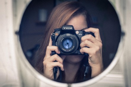 young woman with long hair holding camera over her face